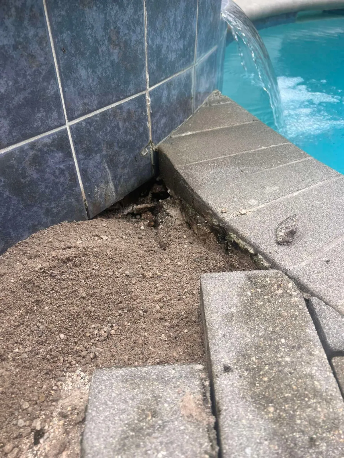 Close-up of pool deck paver repair with base material exposed