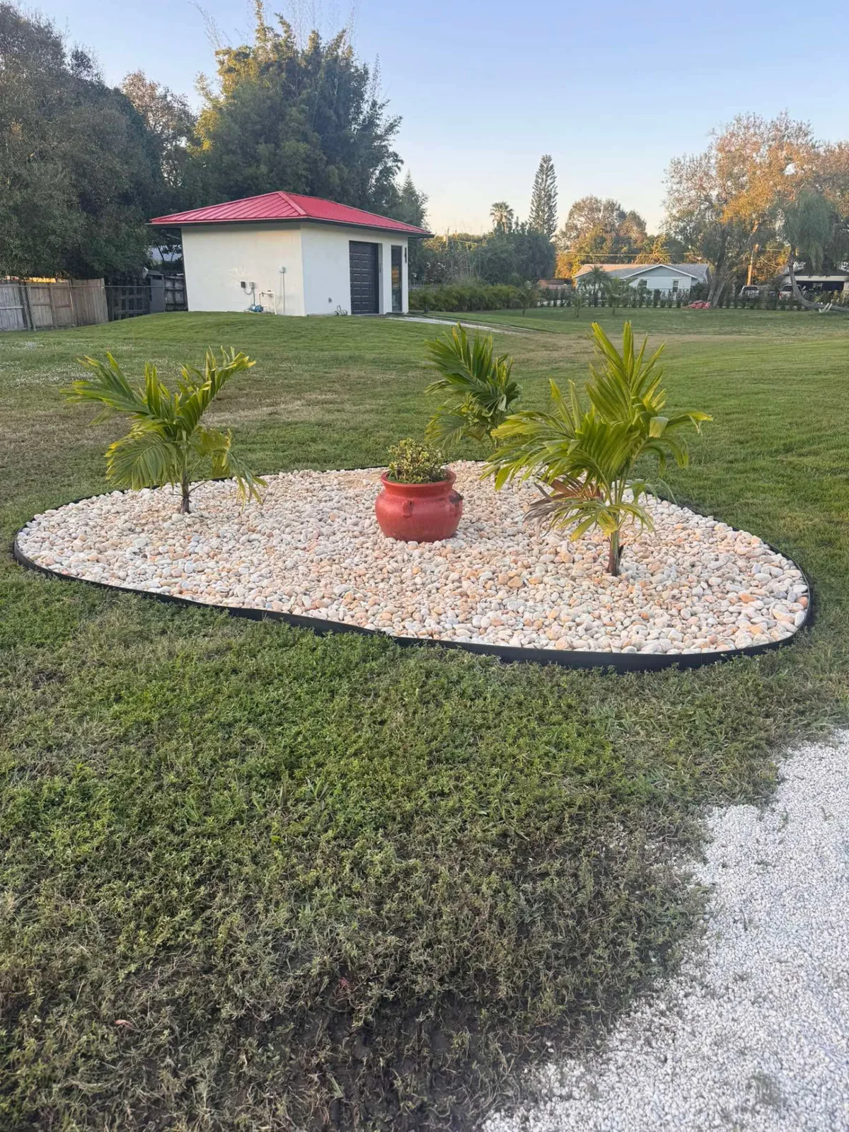 Completed river rock island bed with young palms and a terracotta pot in a large lawn