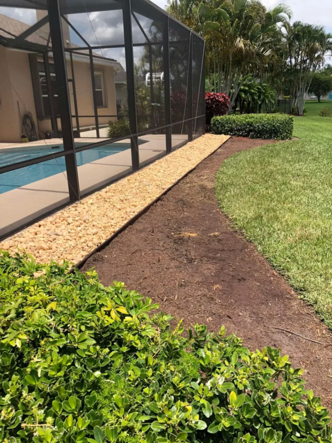 Rock border and prepared soil bed along a pool enclosure during installation