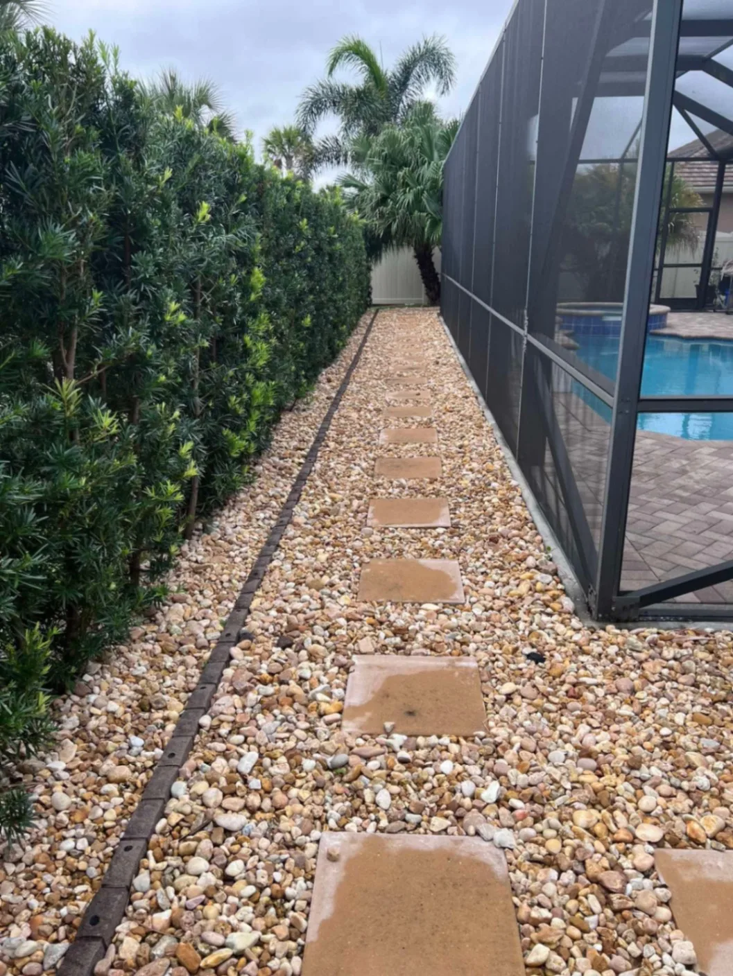 Finished river rock side path with stepping stones between a hedge and a pool enclosure