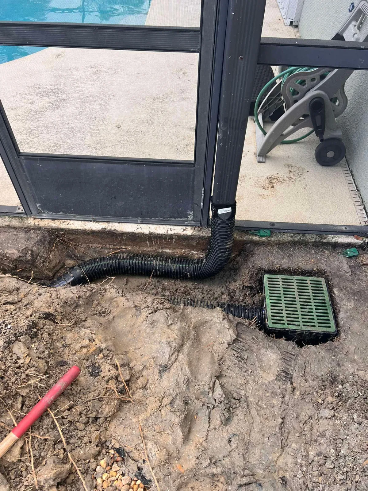 Downspout drainage line connected to a green catch basin beside a pool enclosure