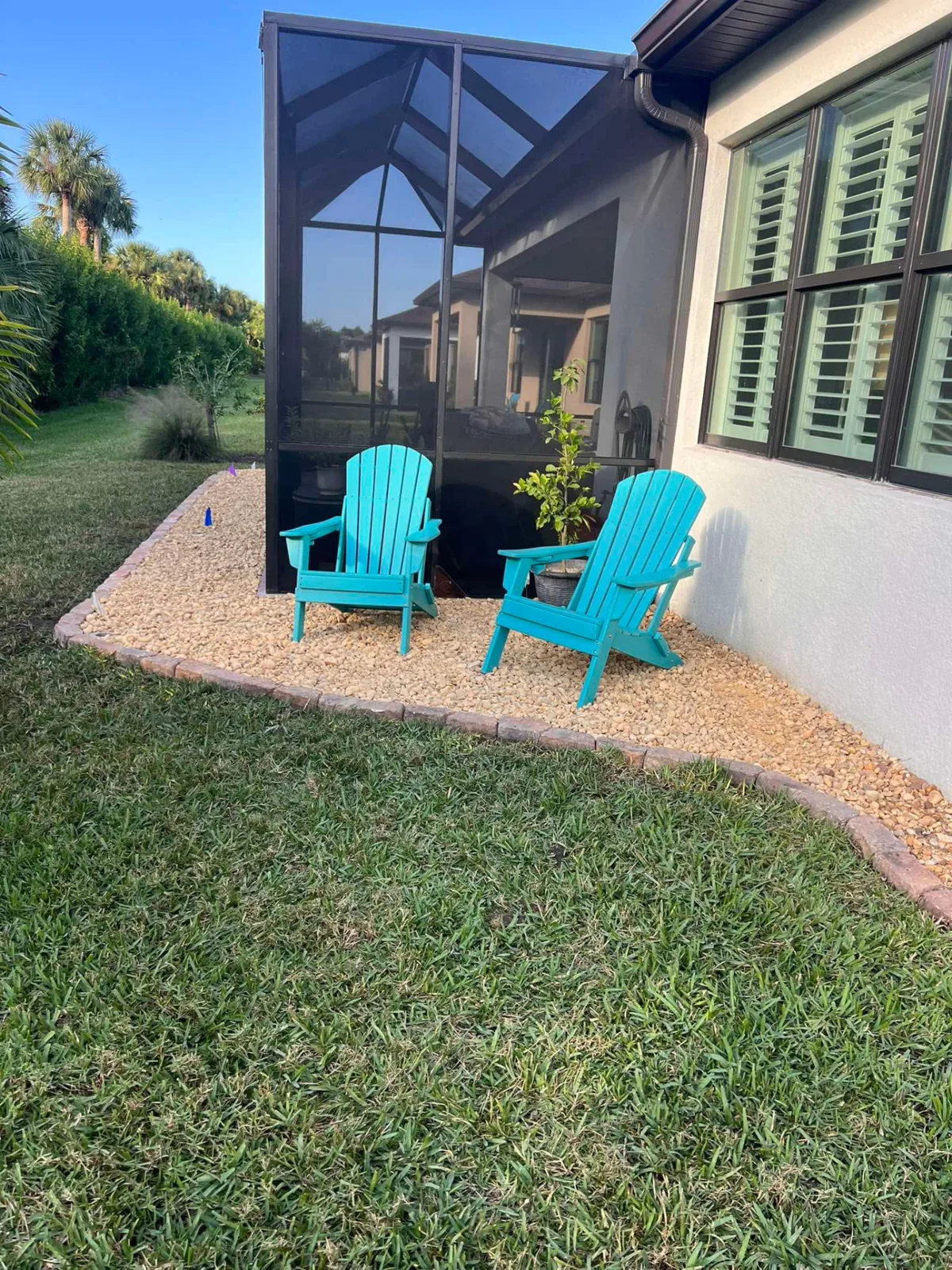 Decorative rock seating area with two Adirondack chairs beside a screened lanai