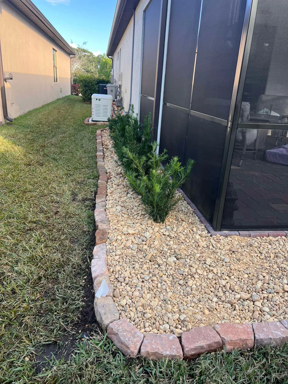 Rock bed with new plantings and paver border along a pool enclosure