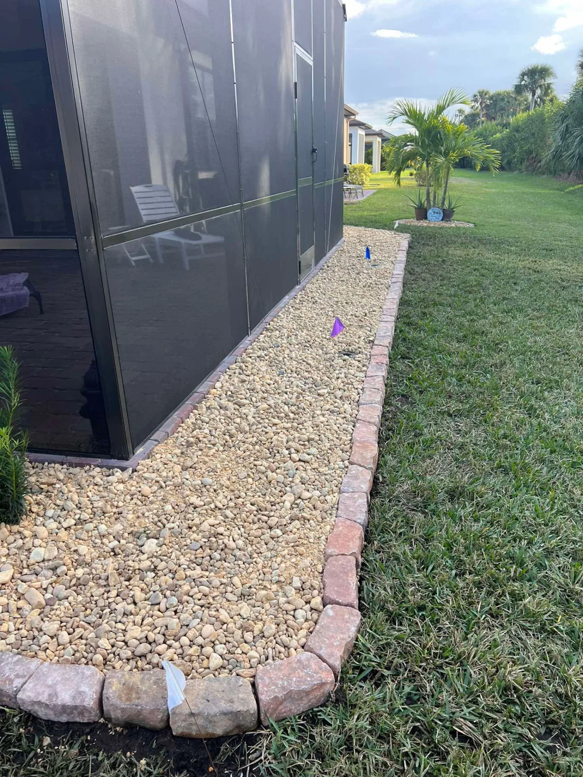 Long decorative rock bed with paver border edging along a pool enclosure